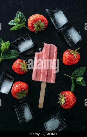 Hausgemachte Erdbeerpopsicles mit Früchten und Eiswürfeln auf dunklem Grund Stockfoto