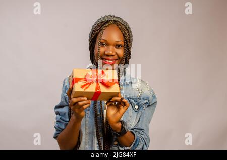 Eine schöne schwarze Frau lächelt, während sie ein Geschenk in ihren Händen hält Stockfoto