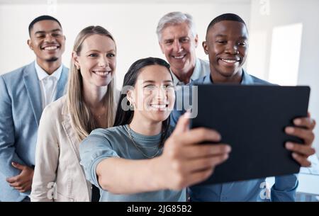Versammeln Sie sich für ein Teamfoto. Aufnahme einer Gruppe von Geschäftsleuten, die zusammen Selfies auf einem digitalen Tablet in einem Büro machen. Stockfoto
