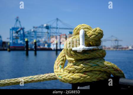 Ein Bügeleisen Poller mit einem gebundenen Seil auf einem Kai im Hafen von Rotterdam in den Niederlanden. Im Hintergrund leicht unscharf, ist die industrielle sind Stockfoto