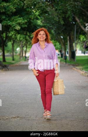 Ganzkörperportrait im Freien mit lächelnder, reifer Rotschopf-Frau. Stockfoto