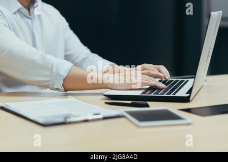 Nahaufnahme der Hände eines Geschäftsmanns, der auf einer Laptop-Tastatur arbeitet und tippt, eines Managers, der im Büro an einem Tisch arbeitet. Stockfoto