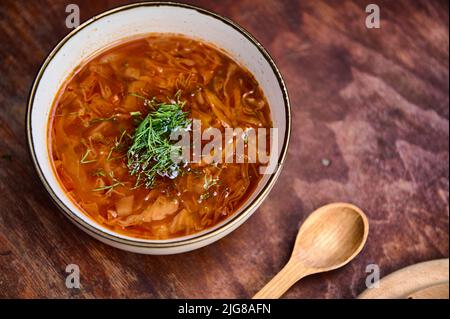 Ukrainischer Borscht serviert in einer Schüssel mit Dill und Petersilie auf einem rustikalen Holztisch. Borscht traditionelle Rote Bete Suppe, ukrainische und russische nationale c Stockfoto