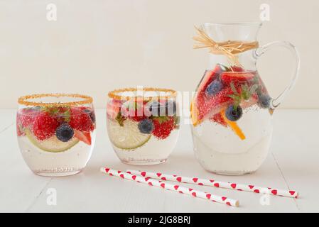 Hausgemachte Limonade mit frischen Sommerbeeren im Krug und 2 Gläser auf weißem Holztisch, keine Menschen, Blick aus der Vogelperspektive. Stockfoto