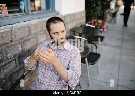 Ein junger Kaukasusmann, der Kaffee in einem Café im Freien trinkt Stockfoto