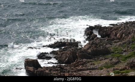 Ein malerischer Blick auf die Wellen des Ozeans, die an einem sonnigen Tag gegen den felsigen Strand krachen Stockfoto