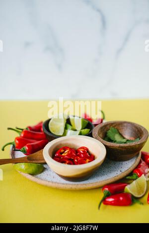 Ein Teller mit Chilischoten, Koriander und Limette in kleinen Schüsseln für Thai-Suppe auf der gelben Theke Stockfoto