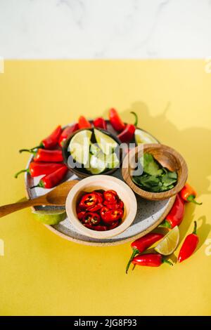 Ein Teller mit Chilischoten, Koriander und Limette in kleinen Schüsseln für Thai-Suppe auf der gelben Theke Stockfoto