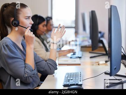 Bereitstellung der besten Lösung und Richtung. Aufnahme einer jungen Callcenter-Agentin, die in einem Büro mit ihren Kollegen im Hintergrund arbeitet. Stockfoto