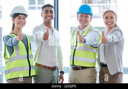 Unterstützung des Builds. Zugeschnittenes Porträt von vier Bauarbeitern, die Daumen nach oben zur Kamera geben. Stockfoto