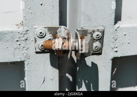 Alte rostige Schraube mit Schraubenmutter, die wie ein Schloss am Metalltor verwendet wird. Stockfoto