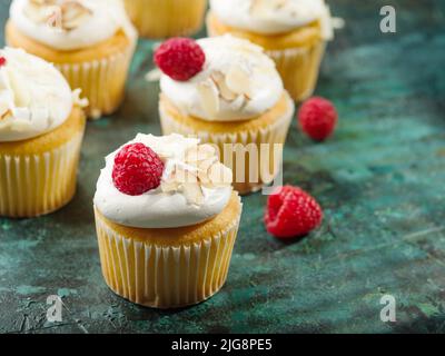 Auf dunkelgrünem Hintergrund Muffins mit Creme, verziert mit frischen Himbeeren und Mandelstücken. Leichtes Sommerdessert. Feiertag, Geburtstag, Bankett, Stockfoto