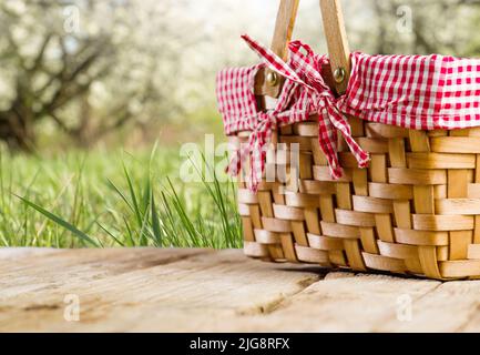 Sommerurlaub, Picknick. Auf einem Holztisch ein Strohpicknickkorb vor dem Hintergrund der Natur, grünes Gras, Bäume. Familienurlaub, Urlaub mit Stockfoto