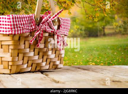 Vor dem Hintergrund der schönen Herbstnatur, ein Picknickkorb auf einem einfachen Holztisch. Landhausstil. Urlaub und Picknick-Konzept. Familienurlaubhaus Stockfoto