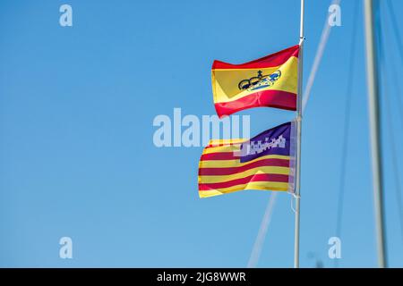 Spanien, Balearen, Mallorca, Bezirk Felanitx, Portocolom. Flaggen von Spanien und Balearen Inseln auf einem Boot, das an der Bucht festgemacht ist, bewegt vom Wind Stockfoto