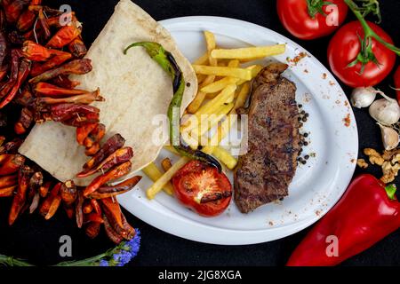 Portionen gegrilltes Filetsteak, serviert mit Tomaten und gebratenem Gemüse auf einem Teller Stockfoto