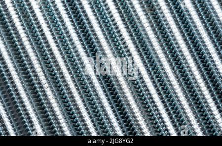 Die Gewindebolzen werden nebeneinander gestapelt, um eine abstrakte Struktur zu schaffen. Vergrößerte Gewindestangen aus Metall. Abstrakter Metallhintergrund. Stockfoto