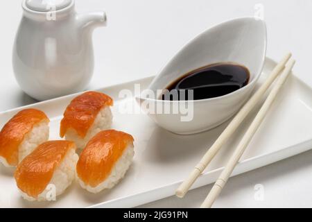 Sushi mit Lachs, Sojasauce in einer weißen Schüssel, Soße und Essstäbchen. Draufsicht. Weißer Hintergrund Stockfoto