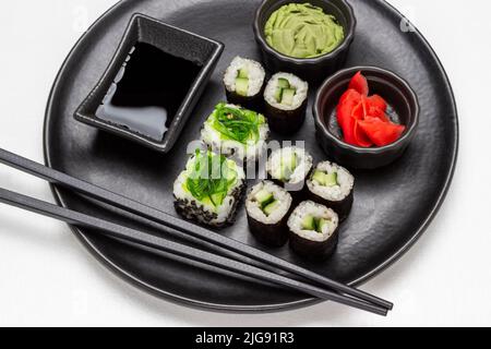 Sushi-Set, Wasabi, Sojasauce und schwarze Essstäbchen auf schwarzem runden Teller. Flach liegend. Weißer Hintergrund Stockfoto