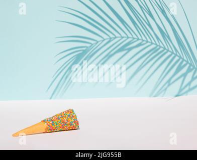 Palmenblatt Schatten und bunte Eis Kegel mit Streuseln auf pastellblauem Hintergrund. Tropisches Sommerkonzept. Stockfoto