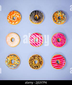 Set von 9 verschiedenen bunten Donuts isoliert auf violettem Hintergrund. In Glasur, mit Schokolade, mit Streuseln, Topping, Marshallows, Haselnuss. Minimal f Stockfoto