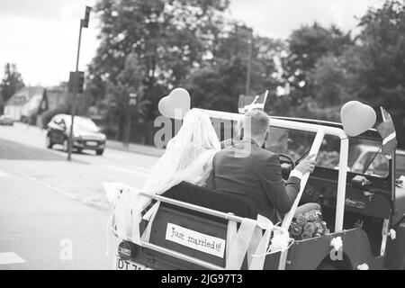 Eine Graustufen-Rückansicht von Braut und Bräutigam auf einem kleinen Auto mit gerade verheirateten Zeichen auf der Rückseite Stockfoto