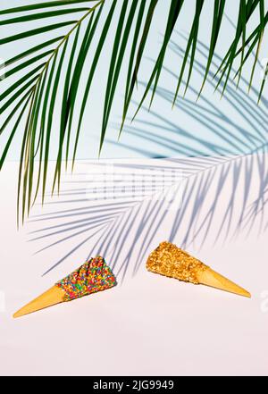 Palmenblatt und bunte Eiszapfen auf pastellblauem Hintergrund. Tropisches Sommerkonzept. Stockfoto