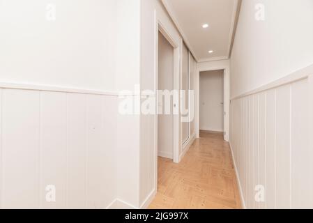 Korridor eines Hauses mit mehreren Türen und Zugang zu verschiedenen Räumen, alle in weißen und holzähnlichen Steinzeugböden Stockfoto