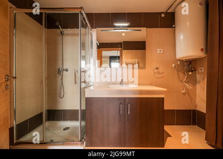 Badezimmer mit dunklen Holzmöbeln, rahmenlosem Spiegel und quadratischer Dusche aus Glas und Chrom-Metall Stockfoto