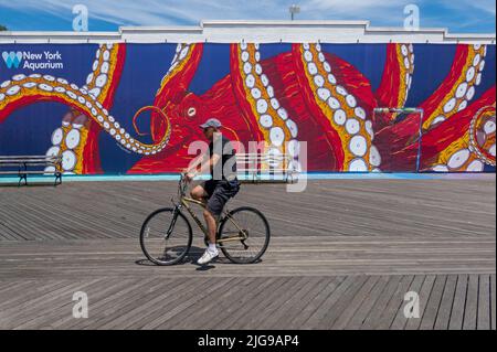 Mann, der mit dem Fahrrad vor dem New York Aquarium Schild auf der Promenade in Coney Island NYC fährt Stockfoto