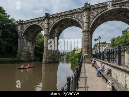 Eisenbahnviadukt über den Fluss Nidd in Knaresborough von unten betrachtet mit Menschen in Booten und Menschen, die von der Uferpromenade aus beobachten Stockfoto