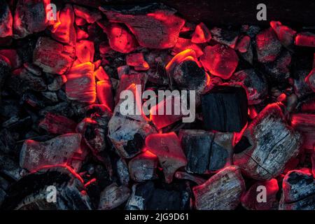 Aktiv schwelende Feuerglut. Hintergrund brennender heißer Kohlen. Flackern brennender Kohlen in der Nacht Stockfoto