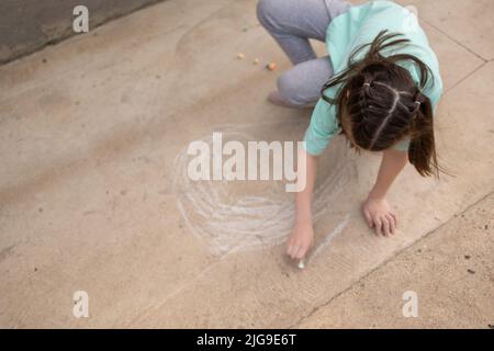 Mädchen zeichnet mit bunten Buntstiften auf dem Bürgersteig. Kinderzeichnungen mit Kreide an der Wand. Kreatives Kind. Freude an der Kindheit. Hochwertige Fotos Stockfoto