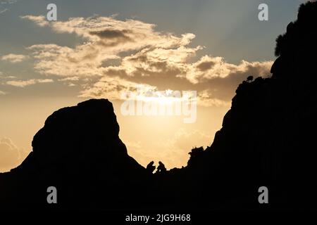 Isolierte Silhouette von zwei Bergsteigern in der Ferne im Hintergrund in hohen Berg bei Sonnenuntergang. Wandern mit unerkennbarem Paar. Konzept von Stockfoto