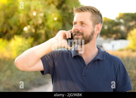 Junger kaukasischer Mann lächelt glücklich mit dem Smartphone im Park. Stockfoto
