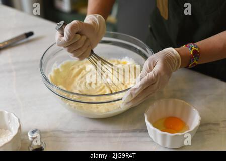 Hände in Gummihandschuhen, die Teig für einen Kuchen rühren Stockfoto