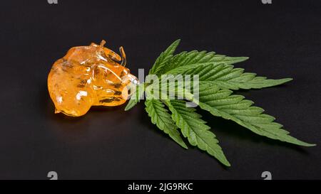 Hoher thc-Gehalt, Stücke von goldgelbem Cannabiswachs und grünem Blatt, Marihuana konzentrieren sich auf dunklen Hintergrund. Stockfoto