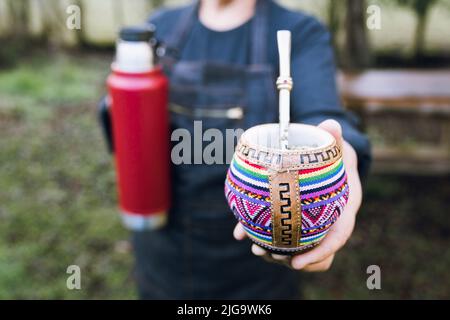 Nicht erkennbare Frau, die ihren Partner mit einer roten Thermo in einem bunten ethnischen Kumpel bedient. Stockfoto