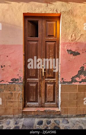 Alte beschädigte Holztür eines verwitterten Gebäudes. Vintage gebrochener und gealterter Eingang zu einem Haus in einem kleinen Dorf oder unten an einem sonnigen Tag Stockfoto