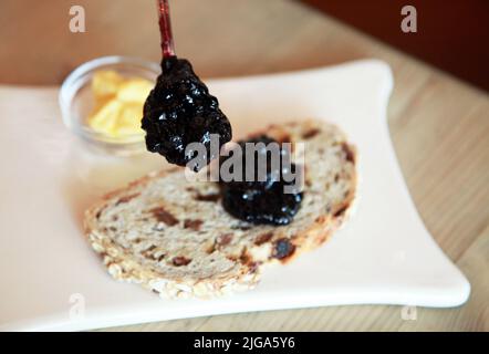 Heidelbeermarmelade und Butter mit Rosinenbrot auf dem Frühstücksteller. Stockfoto