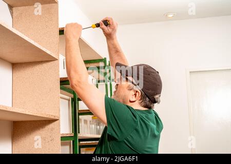 Professioneller Tischler, der mit einem Schraubendreher ein Holzregal in einem Geschäft zusammenführt. Konzept der Arbeit, Baumeister, Arbeiter. Stockfoto