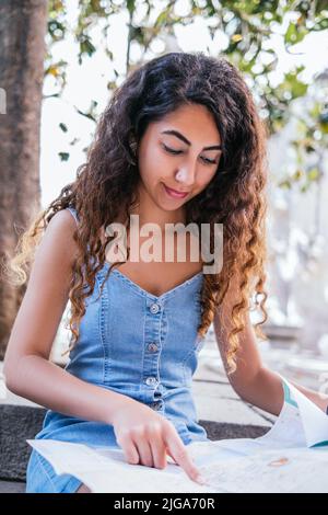 Indische Touristenin, die Papierkarte überprüft und an einem sonnigen Tag auf der Straße der Altstadt auf einer Treppe sitzt Stockfoto