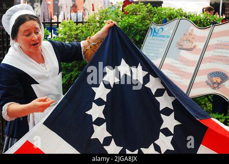 Ein Betsy Ross Reenactor entfaltet eine frühe amerikanische Flagge und zeigt, wie die Näherinnen die Flagge in Philadelphia entworfen und geschaffen haben Stockfoto