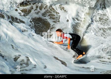 Ein junger erwachsener kalifornischer Surfer fängt die perfekte Welle ein, als er auf seinem Surfbrett im Meer durch das Wasser schneidet. Stockfoto