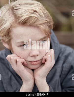 Einsames Kind mit den Händen am Kinn denkend. Junge kleine Teenager-Kind draußen auf einem Spielplatz allein. Niedlich kaukasischen männlichen Kind ernst. Gelangweilter Teenager Stockfoto