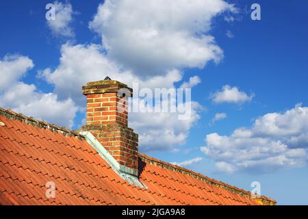 Ein Haus mit einem roten Ziegelkamin auf einem Asbestschieferdach draußen mit einem blauen Himmel Hintergrund. Außengebäude entworfen Konstruktion und Stockfoto