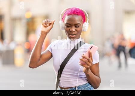 Afrikanische Frau tanzt, während sie mit Kopfhörern im Freien Musik hört Stockfoto