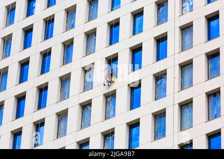 Gruppe von Fensterscheiben, die an Seilen an einer Wolkenkratzerfassade hängen Stockfoto