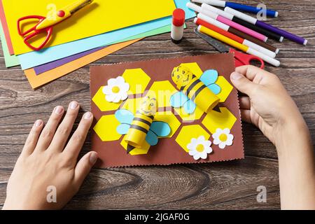 Das Kind hält eine Sommerkarte mit voluminösen Bienen. Handgefertigt. Kinderkreativitätsprojekt, Basteln für Kinder. Stockfoto