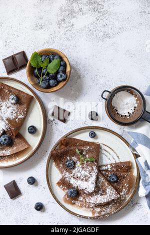 Wir feiern den Pfannkuchen-Tag, ein gesundes Frühstück. Köstliche hausgemachte Schokoladencrepes mit Heidelbeeren auf einer Steinplatte. Blick von oben. Speicherplatz kopieren. Stockfoto